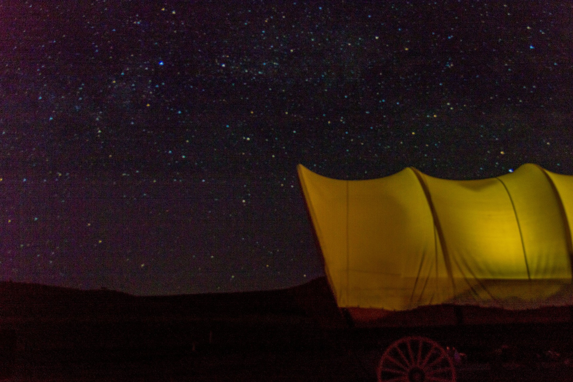 Glamping Camping Wagon Set up at a Mountain Lake and Glowing under the Night Sky and Stars